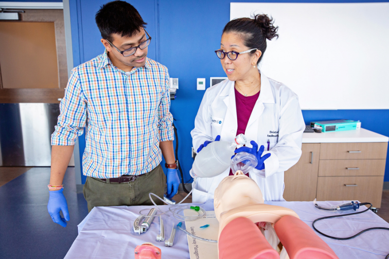 a student observes a teacher doing a demonstration on a medical dummy.