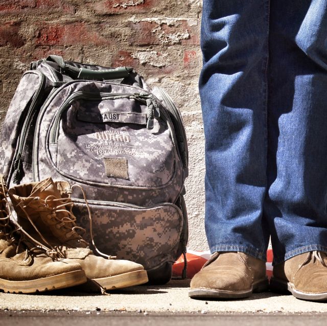 A pair of legs standing next to boots and a backpack
