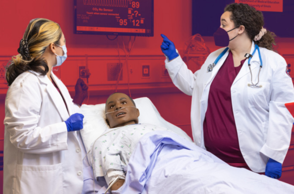 Two doctors with a dummy patient in a simulation lab looking at the vitals on a monitor