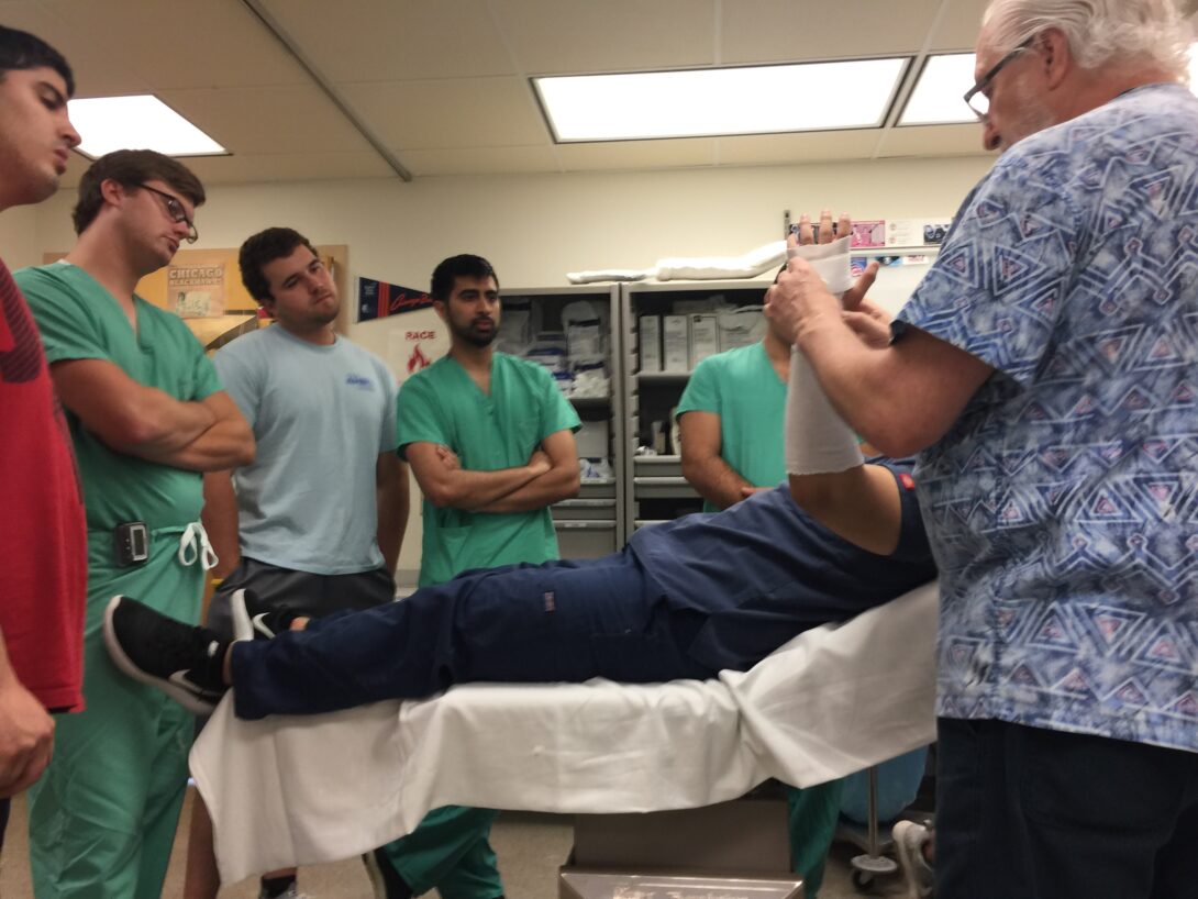 Students in scrubs stand around a patient on an exam table