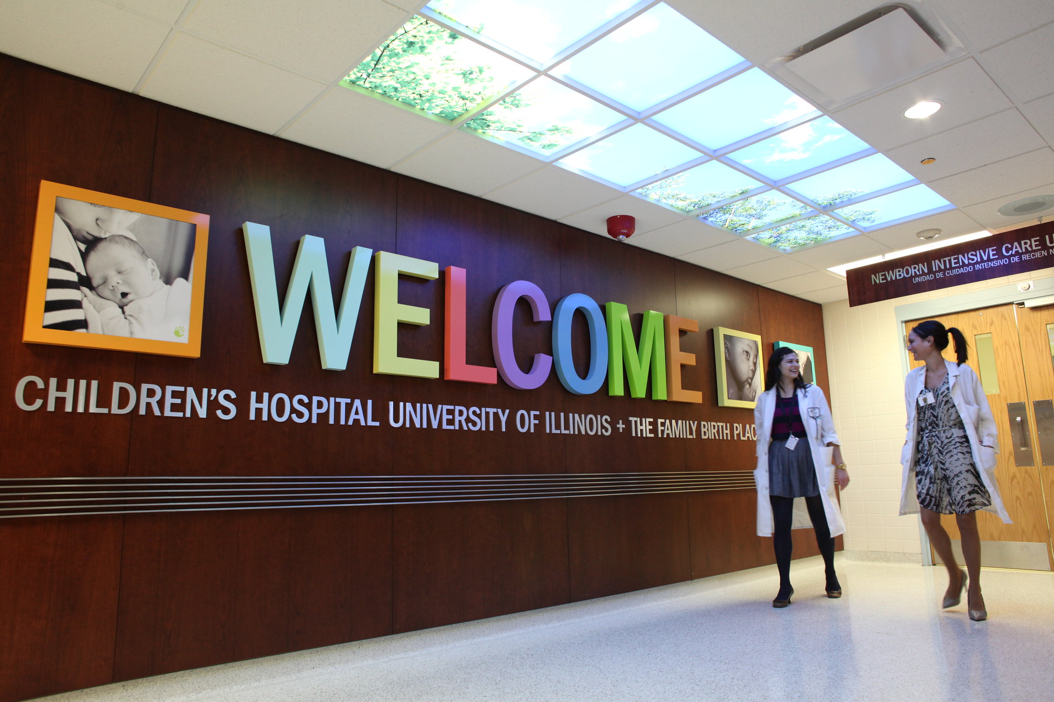 A doctor stands in front of a big sign welcoming visitors to the hospital.