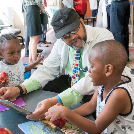 A doctor kneels down and talks with two children.