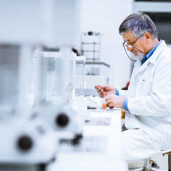 A lab worker in a white coat works at a table.