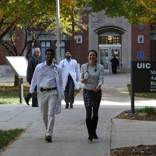 3 doctors walk down the sidewalk outside a campus building